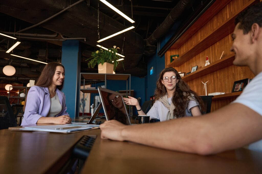 Business meeting in Southlake, TX, with two women and one man discussing a project on a laptop at a table in a modern office space.